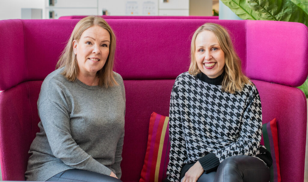 two women sitting on a pink sofa